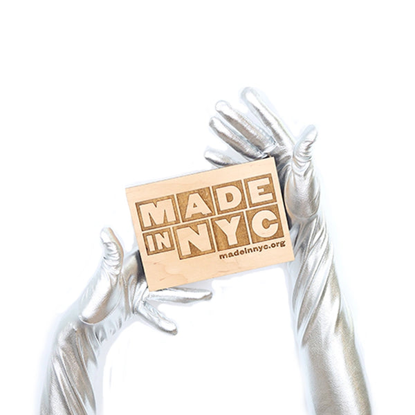 opera length metallic black vinyl gloves holding a wooden Made in NYC sign