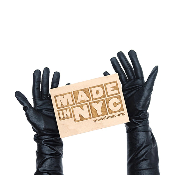 opera length metallic black vinyl gloves holding wooden Made in NYC sign