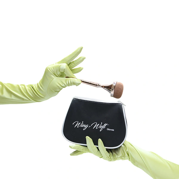 opera length shiny light yellow vinyl gloves with a makeup brush in left hand and makeup pouch in right hand