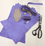 photograph of purple fabric glove cutouts, strips of purple and tan fabric, white measuring tape, purple thread, a clear ruler and black scissors
