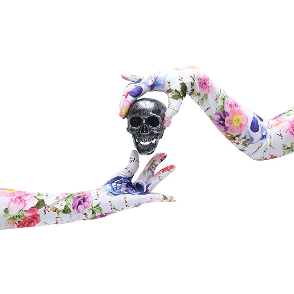 hands wearing long floral skull pattern gloves holding a mini silver skull